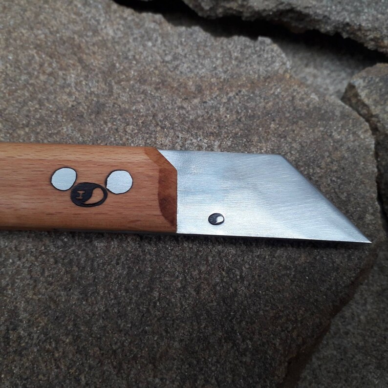 May include: A small, wooden-handled knife with a silver blade. The handle has a carved design of a bear's face with two white circles for eyes.