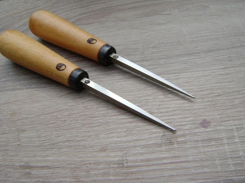 May include: Two wood handled carving tools with metal blades. The tools have a black metal ferrule and a wood handle with a small circle logo.