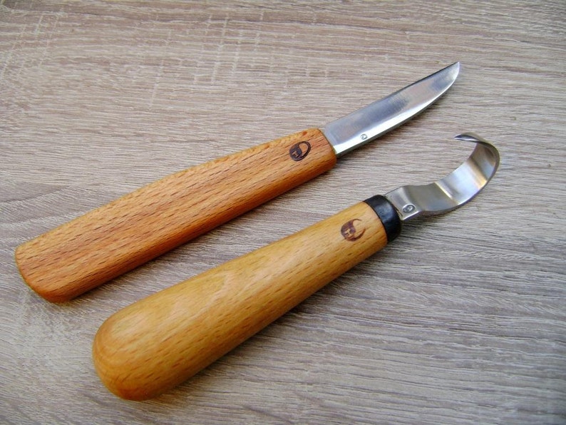 Op de afbeelding: Twee houtsnijgereedschappen met metalen bladen. Het gereedschap aan de linkerkant heeft een gebogen blad en het gereedschap aan de rechterkant heeft een haakvormig blad.