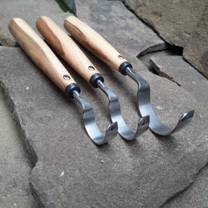 May include: Three wood carving tools with curved blades and wooden handles. The tools are arranged in a row, with the blades facing the viewer.