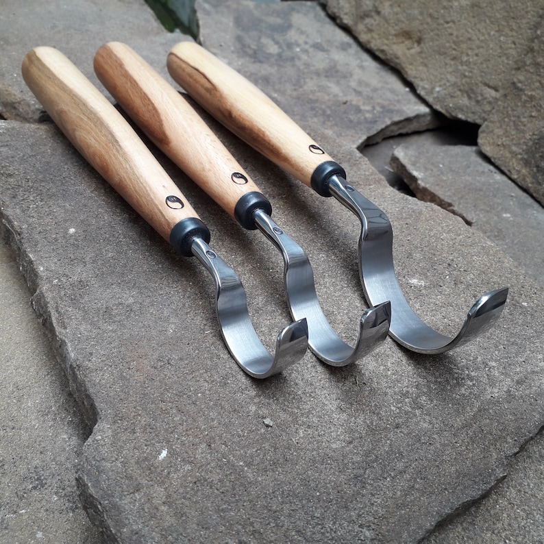 May include: Three wood carving tools with curved blades and wooden handles. The tools are arranged in a row, with the blades facing the viewer.