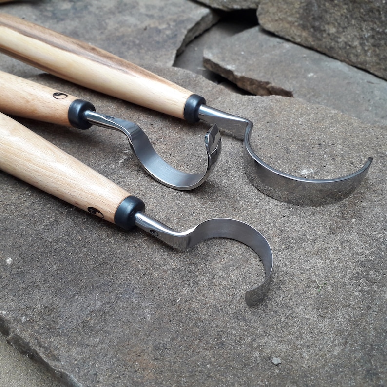 May include: Three wood carving tools with metal blades. The tools have wooden handles and are lying on a rough, gray surface.