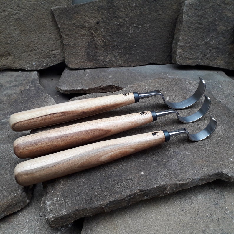 May include: Three wood carving tools with curved blades and wooden handles. The tools are arranged in a row, with the largest tool at the top and the smallest tool at the bottom.