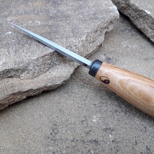 May include: A wood handled carving tool with a silver blade and a black yin yang symbol on the handle.