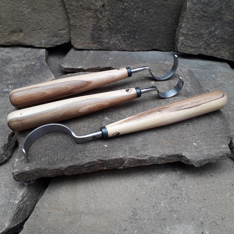 May include: Three wood handled carving tools with curved metal blades. The tools are arranged on a stack of gray rocks.
