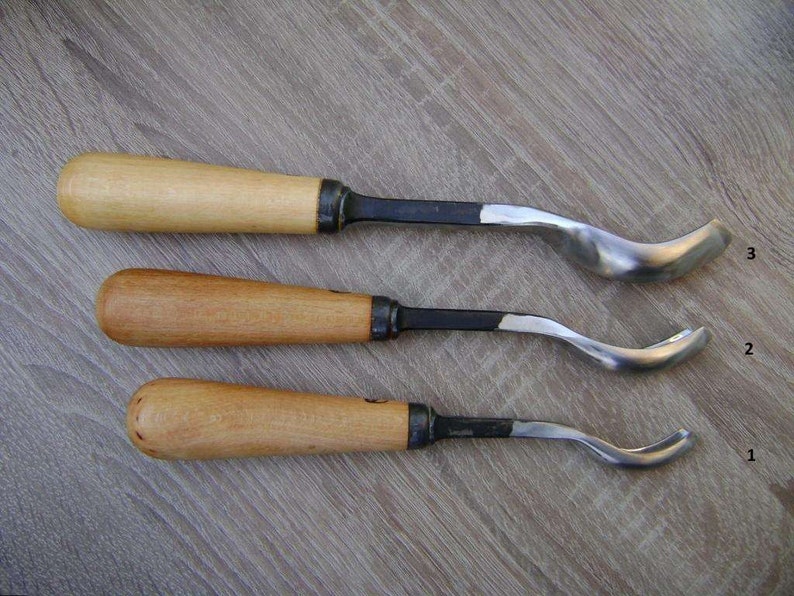 以下が含まれることがあります： 木製のハンドルと湾曲した金属製の刃を持つ木彫りの道具が3つあります。道具は1、2、3と番号が付けられています。