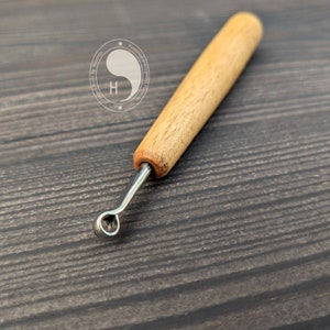 Puede incluir: Una pequeña herramienta de escultura con mango de madera, un bucle de metal y una bola redonda en el extremo. La herramienta está diseñada para crear pequeñas formas detalladas en arcilla u otros materiales blandos.