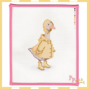 May include: A needlepoint canvas featuring a cross-stitched goose wearing a yellow hooded raincoat and matching yellow rain boots. The white canvas has a pink fabric border and includes a colour palette guide on the right side and the text Pp pearl & point.