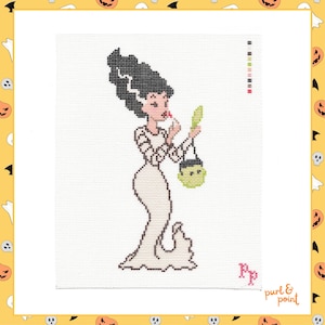 May include: A cross-stitch pattern on white fabric featuring a stylised figure with tall black hair, wearing a long white gown, applying red lipstick while holding a green hand mirror and a small green cauldron-shaped bag, with a colour key.