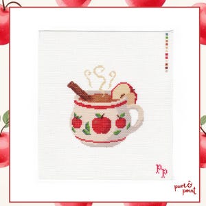 May include: A cross-stitch pattern on white fabric featuring a mug filled with a brown beverage, a cinnamon stick, and an apple slice. The mug is decorated with red apple motifs and green leaves. Steam rises from the top, and the letters PP are stitched.