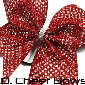 May include: Red glitter cheer bow with silver rhinestones. The bow is tied with a silver ribbon and has a black elastic band.