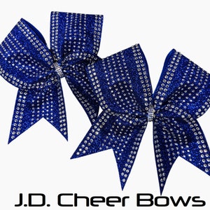 May include: Two royal blue cheer bows with silver glitter and rhinestones. The bows are tied together with a silver ribbon.