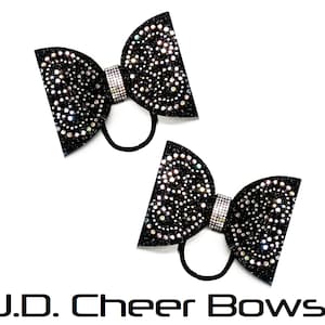 May include: Two black glitter cheer bows with iridescent rhinestones. Each bow has a rhinestone-studded center and a black elastic band. The text "J.D. Cheer Bows" is at the bottom.