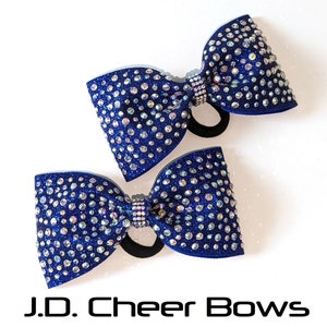 May include: Two blue cheer bows with iridescent rhinestones. The bows are tied with black elastic hair ties.  J.D. Cheer Bows.