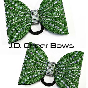 May include: Two green glitter cheer bows with clear rhinestones and a black elastic band.  J.D. Cheer Bows.