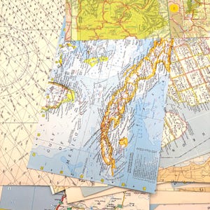 May include: A collage of overlapping paper maps featuring a central map of Cuba and the Gulf of Mexico, a nautical chart with grid lines on the left, and a yellow-toned map of Yellowstone National Park at the top, all layered together.
