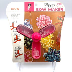 Puede incluir: Un kit vintage "Pixie Bow Maker" en su embalaje original. El kit presenta una herramienta rosa de plástico para hacer lazos con un diseño de hélice, e incluye instrucciones y alfileres para lazos. El embalaje muestra varios lazos coloridos.