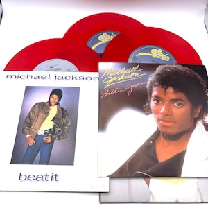 May include: A collection of Michael Jackson vinyl records and album covers. The image features three red vinyl records, and two album covers. One album cover has the text "Beat It" and the other album cover has the text "Billie Jean".