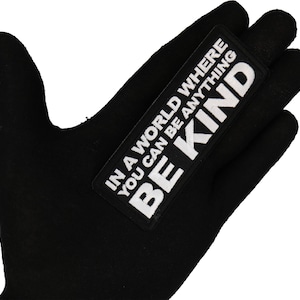 May include: Black fabric patch with white text that reads "In a world where you can be anything, be kind."