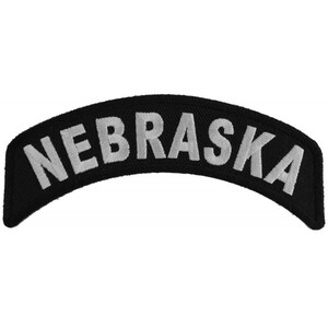May include: Black and white embroidered patch with the word "NEBRASKA" in a white arch on a black background.