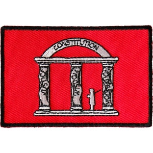 May include: A red rectangular patch with a black border. The patch features a white and gray illustration of a building with three columns. The word "CONSTITUTION" arches above the building. The columns are labeled "JUSTICE", "WISDOM", and "MODERATION".