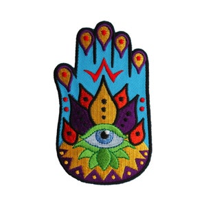 May include: A blue embroidered patch with a stylized hand, a yellow flower with a purple center, and a blue eye in the center of the flower. The hand has red and yellow dots around the fingers.