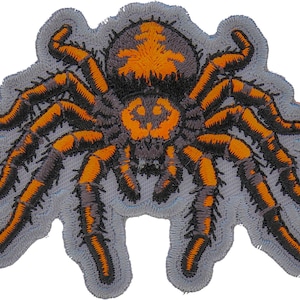 May include: A black and orange embroidered patch of a tarantula spider with hairy legs.