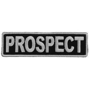 May include: A rectangular black patch with the word "PROSPECT" embroidered in white thread. The patch has a white border and is likely designed to be sewn onto clothing or accessories.