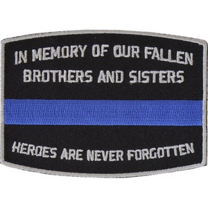 May include: Black embroidered patch with a thin blue stripe in the center. The text reads "In Memory of Our Fallen Brothers and Sisters Heroes Are Never Forgotten."