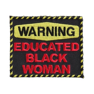 May include: A black fabric patch with yellow and black striped border. The patch has the text "WARNING EDUCATED BLACK WOMAN" in red embroidered letters.