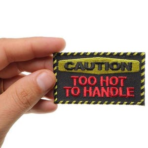 May include: Black and yellow caution patch with the text "CAUTION TOO HOT TO HANDLE" in red and black lettering.