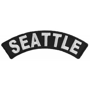 May include: Black and white embroidered patch with the word "SEATTLE" in white lettering on a black background. The patch is curved in the shape of a half-circle.
