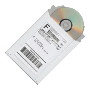 May include: White padded envelope with a USPS First-Class Package label. The label includes the text "USPS First-Class PKG TM" and "Crazy Novelty Guy, Melbourne FL 32936-1044". The envelope contains a silver disc.