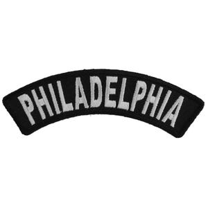 May include: Black and white embroidered patch with the word "PHILADELPHIA" in white lettering on a black background. The patch is curved in a half-circle shape.