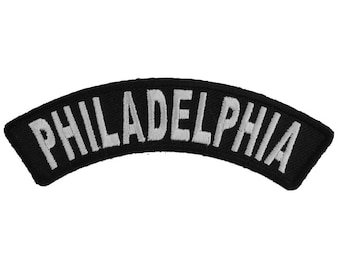May include: Black and white embroidered patch with the word "PHILADELPHIA" in white lettering on a black background. The patch is curved in a half-circle shape.