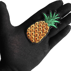 May include: A black fabric patch with an embroidered pineapple design. The pineapple is yellow with green leaves.