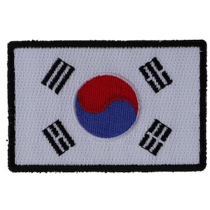May include: A white embroidered patch with the South Korean flag. The flag features a red and blue yin-yang symbol surrounded by four black trigrams.