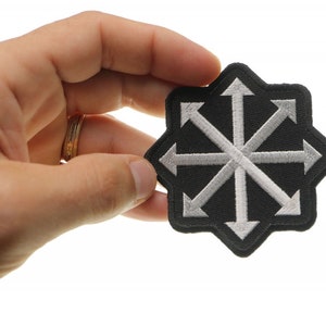 May include: A black and white embroidered patch with a starburst design featuring eight arrows pointing outwards. The patch is edged in black.
