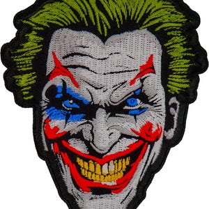 May include: A close-up of a white and grey embroidered patch depicting a grinning clown with green hair, red and blue makeup, and a wide, toothy smile.