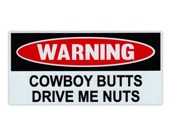May include: A black and white warning sign with red text that reads "WARNING" in a red oval. The text below the oval reads "COWBOY BUTTS DRIVE ME NUTS".