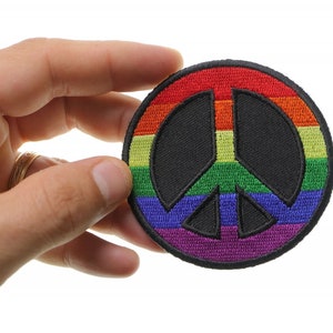 May include: A rainbow peace sign patch with a black outline. The patch is made of fabric and has a stitched design.