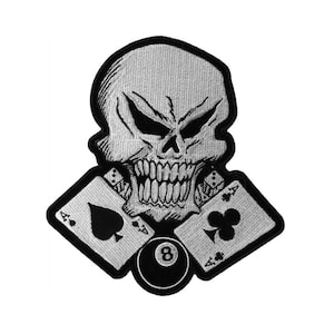 May include: A black and white embroidered patch featuring a skull with a menacing expression, holding two playing cards, an ace of spades and an ace of clubs, and a black 8-ball.