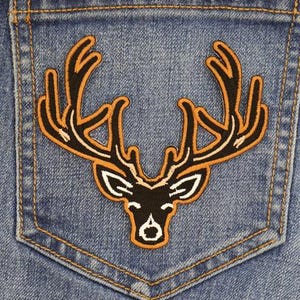 May include: A brown and black deer head patch with antlers, sewn onto a blue denim pocket.