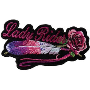 May include: Embroidered patch with the words "Lady Rider" in pink script above a colorful feather and a pink rose. The feather has shades of purple, pink, and white. The patch is on a black background.