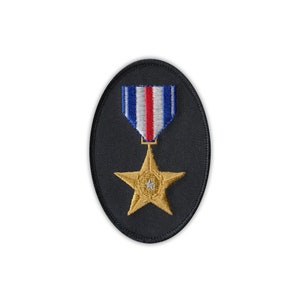 May include: An embroidered patch featuring a gold star pendant suspended from a blue, white, and red striped ribbon. The star is centered on a black oval background. The patch is designed for application on clothing or fabric.