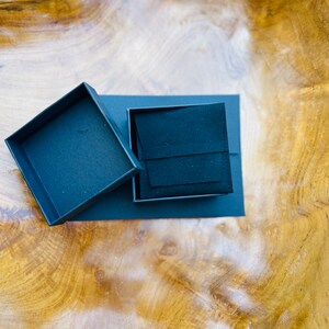 May include: A black square box with a black velvet interior. The box is open and the lid is lying next to it.