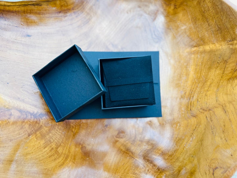May include: A black square box with a black velvet interior. The box is open and the lid is lying next to it.