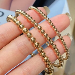 May include: Three gold beaded bracelets of varying sizes stacked on top of each other.