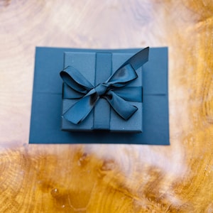 May include: A black gift box with a black ribbon tied in a bow.