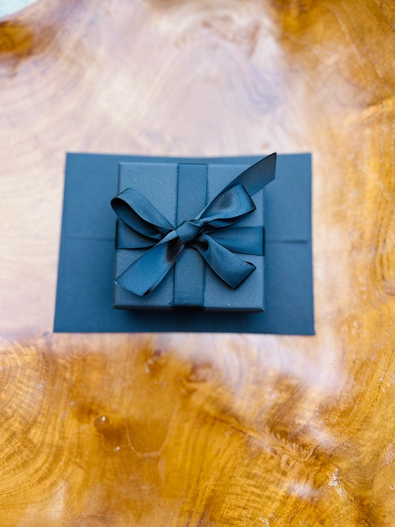 May include: A black gift box with a black ribbon tied in a bow.